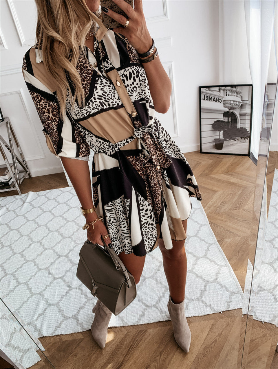 Woman taking a mirror selfie wearing a patterned dress and holding a handbag in a room with wooden flooring.
